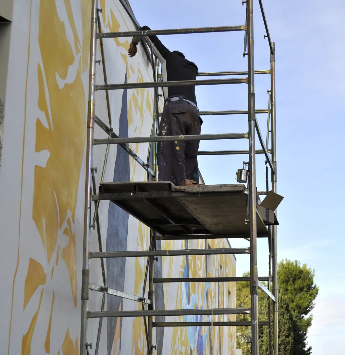 L’artista dipinge il murale da un ponteggio